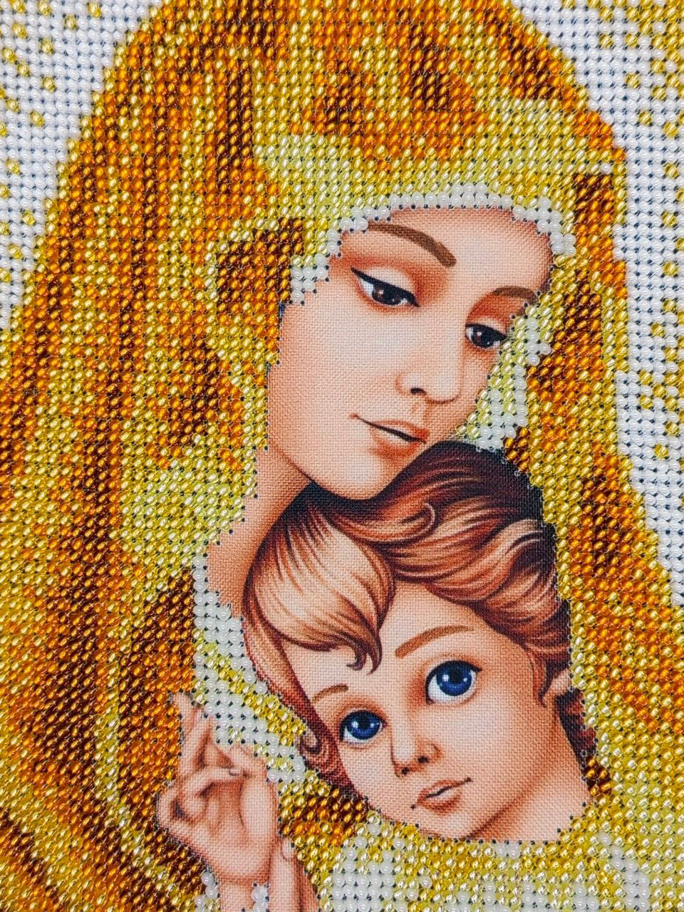 Detailed view of the Virgin Mary's face and the Christ Child's blue eyes surrounded by gold and ivory bead embroidery.
