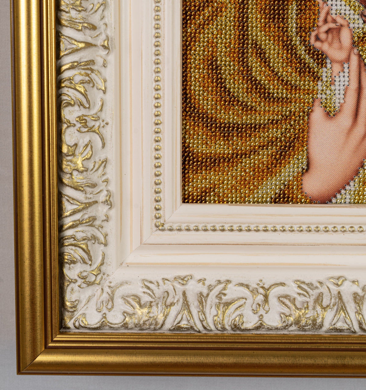 Close-up of the ornate ivory-and-gold frame surrounding the Gold Madonna bead embroidery, showing raised details