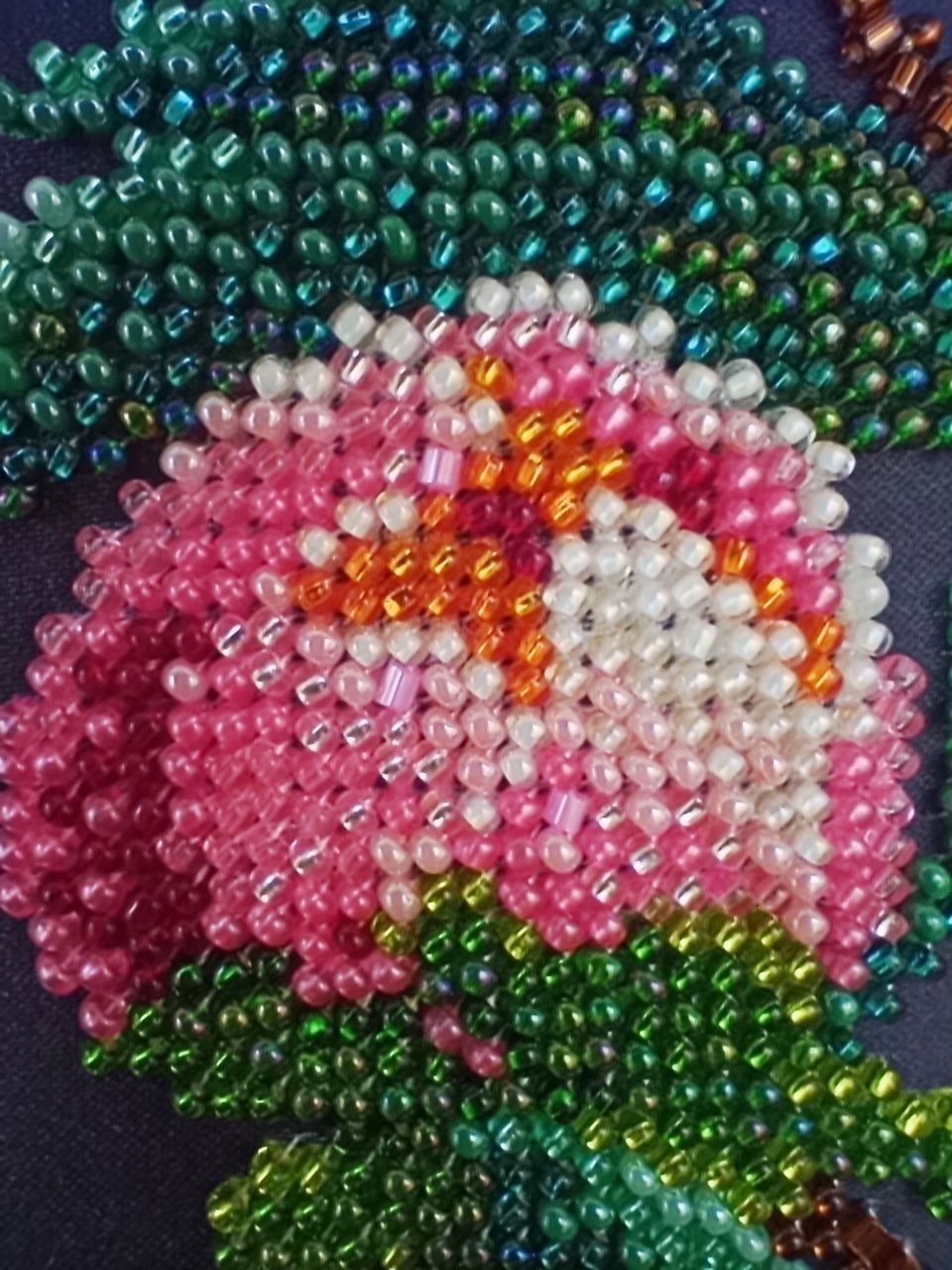 Extreme close-up of hand-beaded peony bud, branches and green foliage