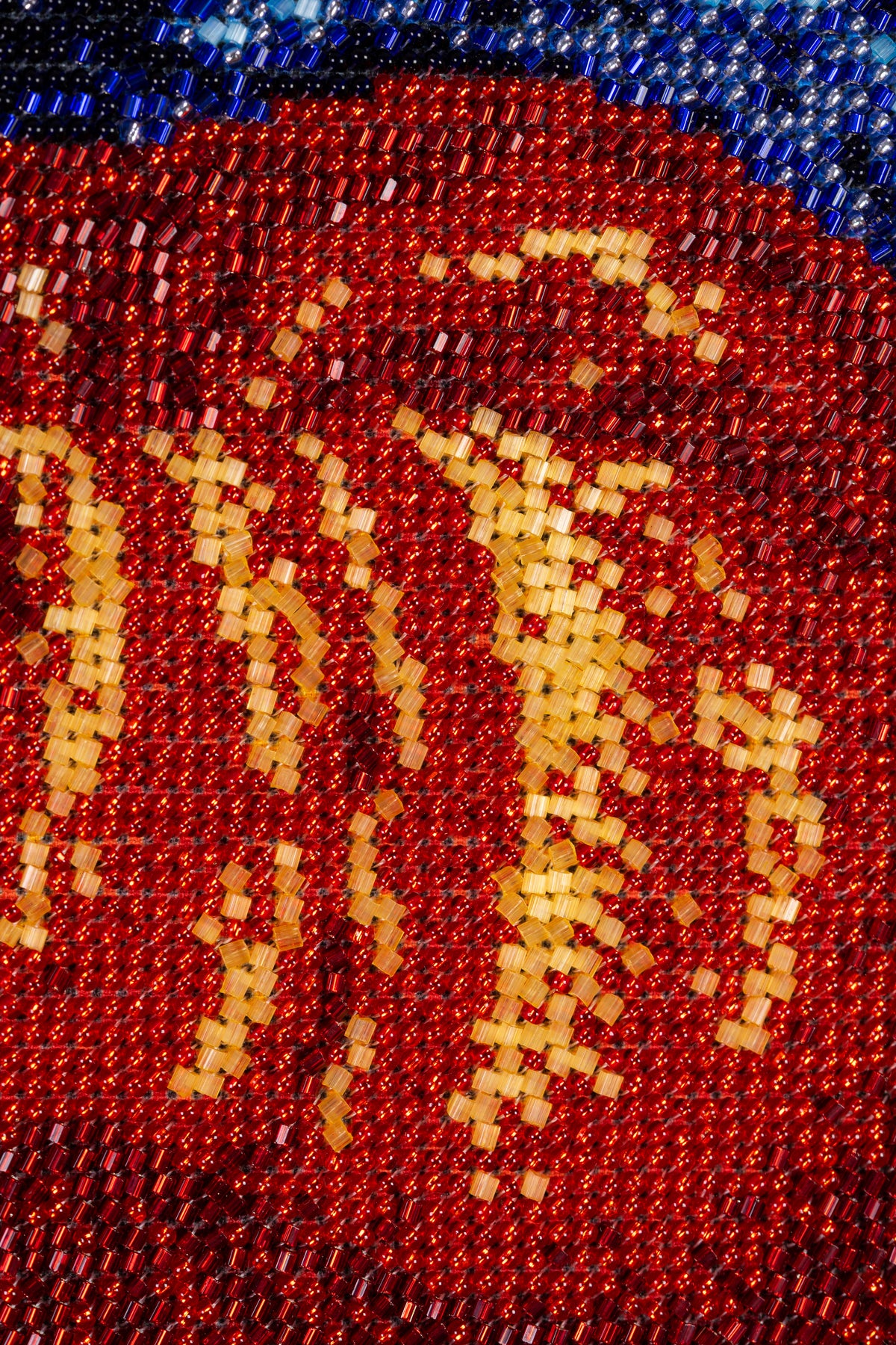 Macro detail of red and gold glass bead embroidery on the Madonna’s garment