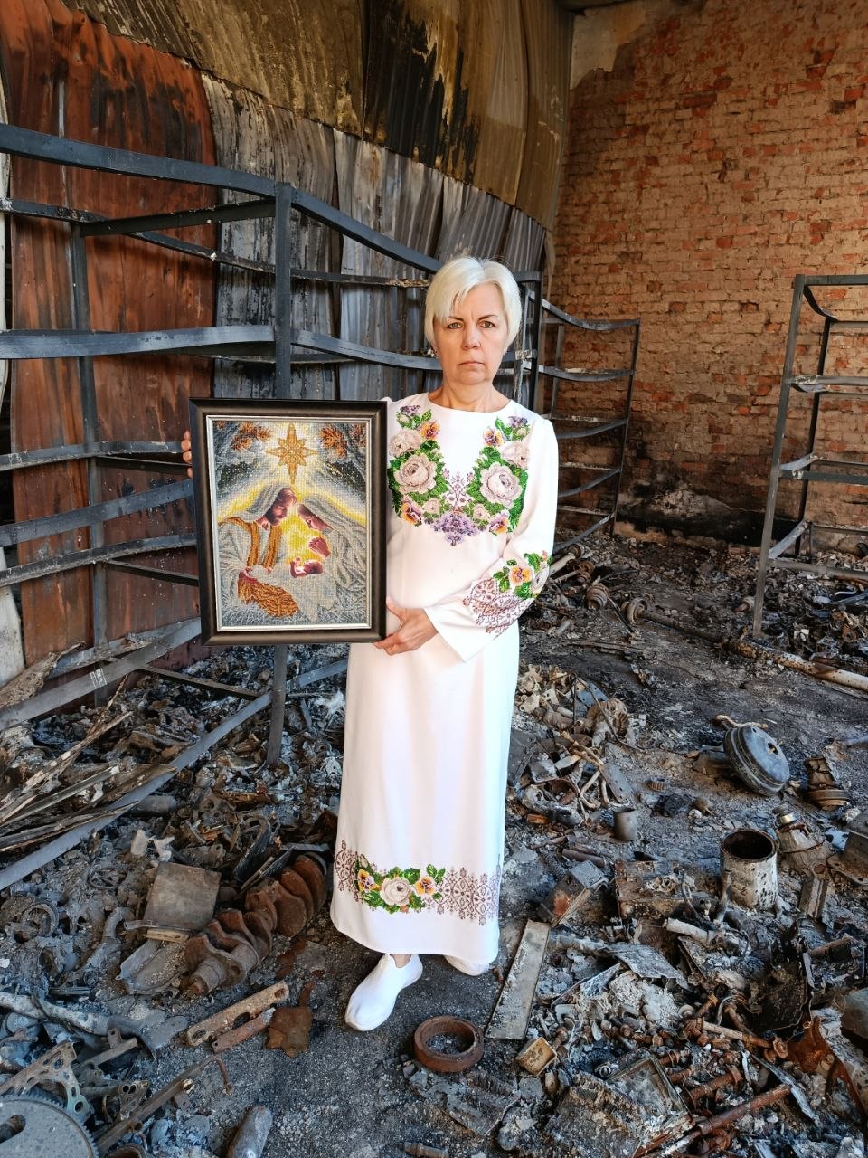 Ukrainian artist Raisa Yevtushenko holding her bead-embroidered artwork Incarnation inside a war-damaged building in Ukraine