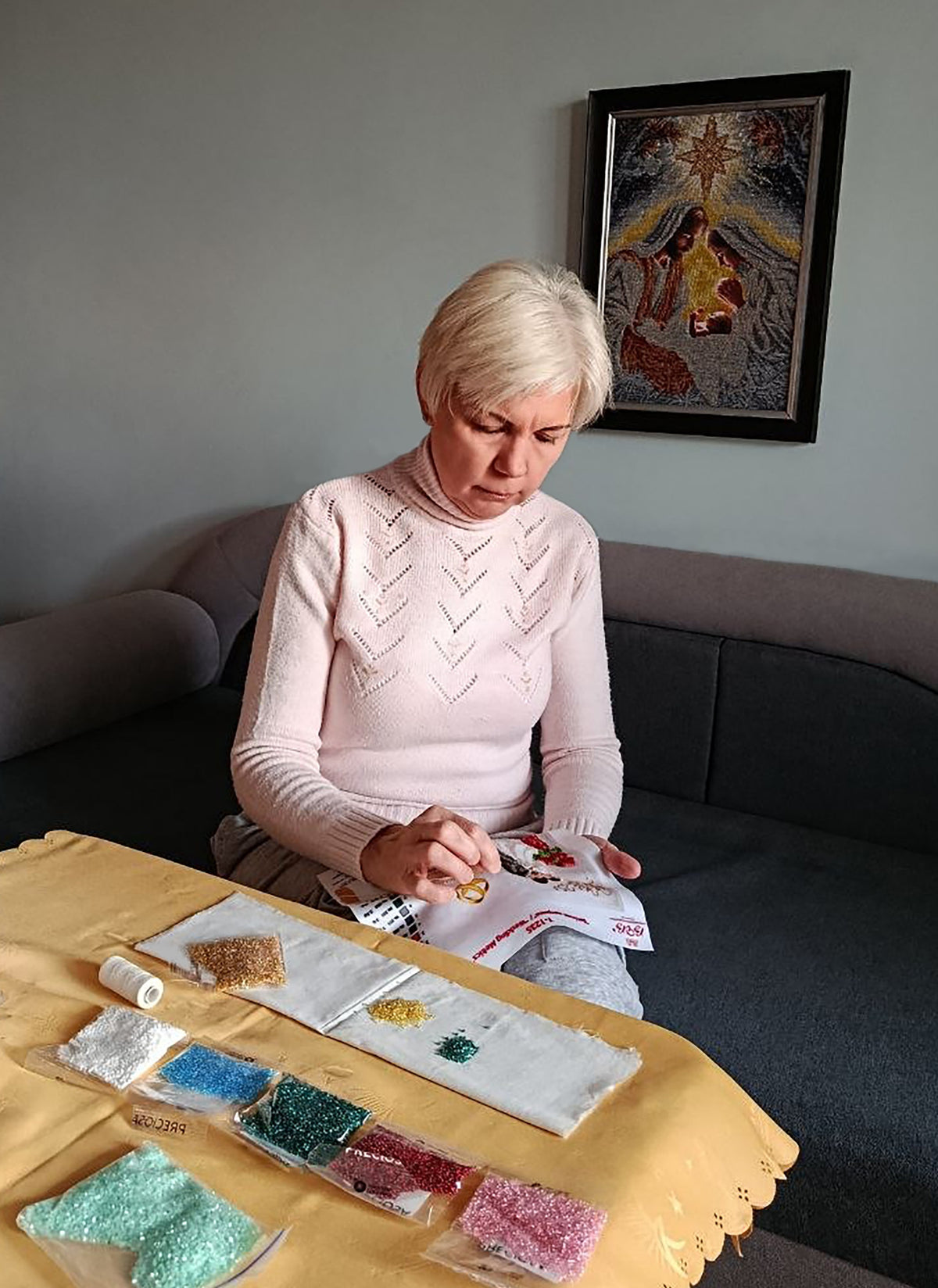 Artist Raisa Yevtushenko creating bead embroidery by hand in her home workspace, surrounded by glass beads and materials