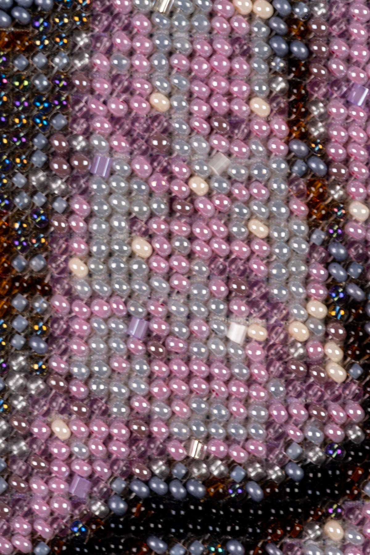 Extreme macro of pink, grey, ivory and transparent seed beads showing the texture and precision of the hand embroidery