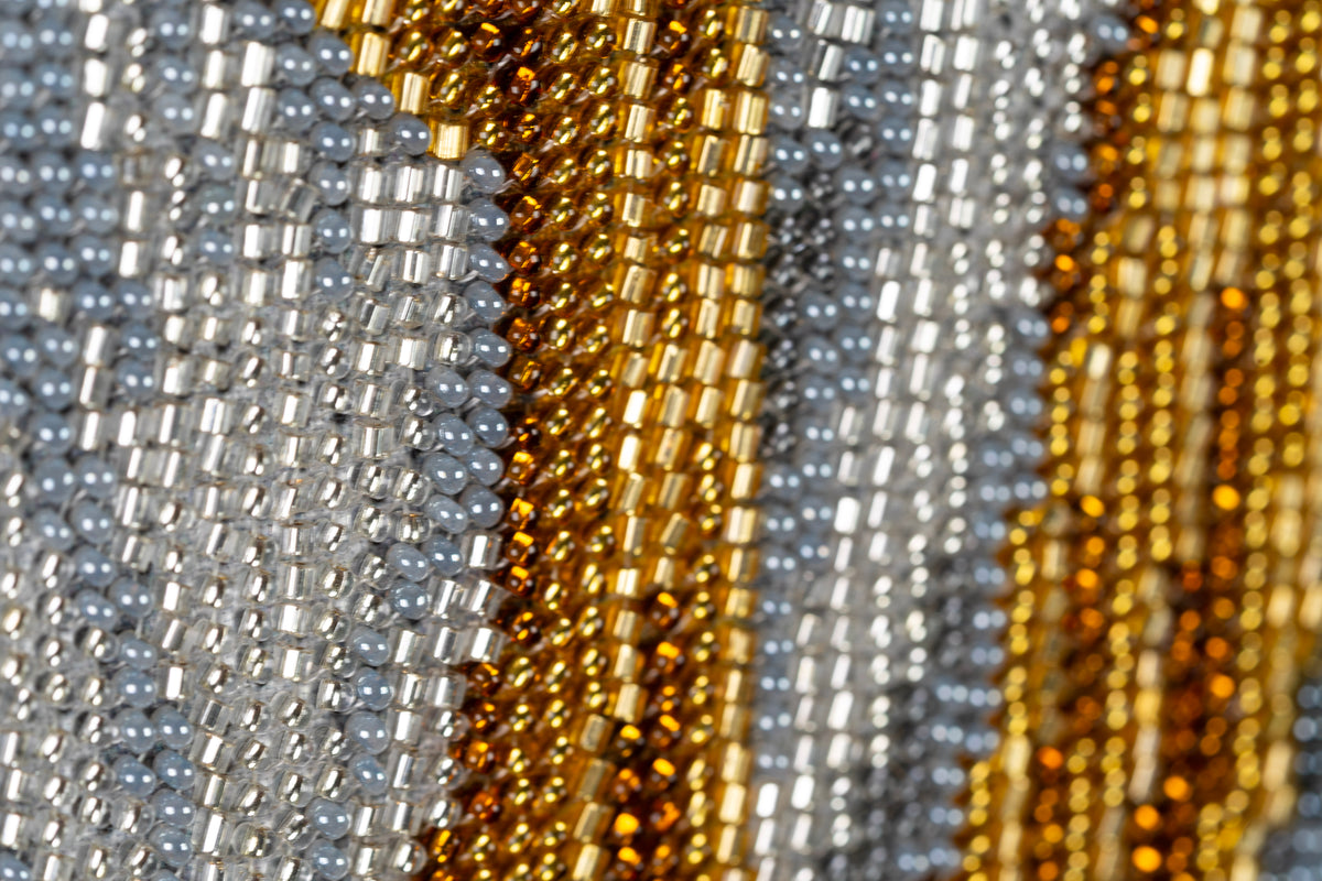 Close-up of gold and amber bead embroidery in Incarnation showing the hand-stitched surface and tonal transitions