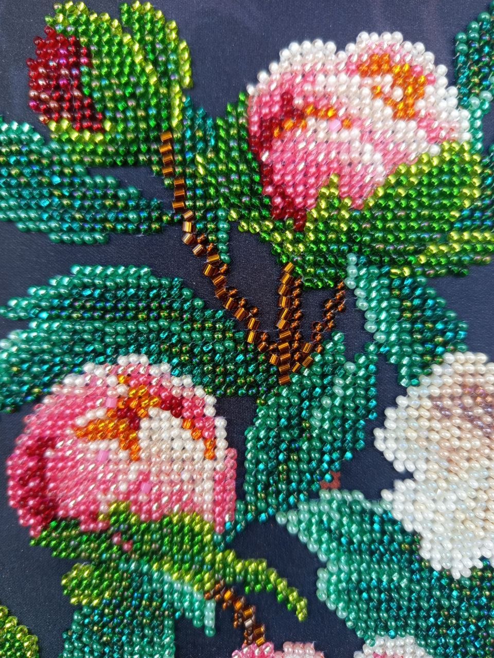 Close-up of hand-beaded peony buds, branches and green foliage against the dark textile background