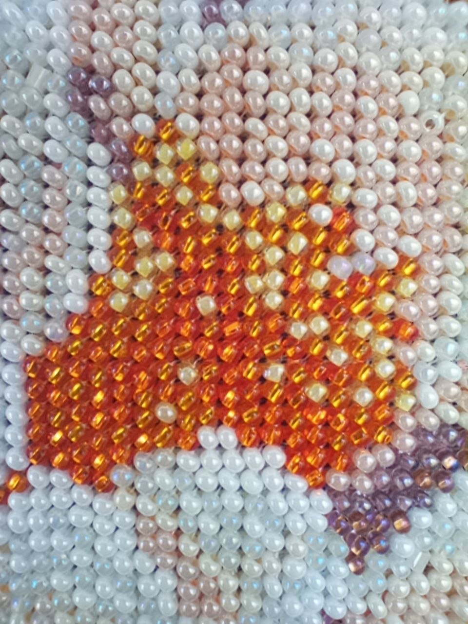 Extreme close-up of glass bead embroidery showing the orange centre and pale petals of a peony flower