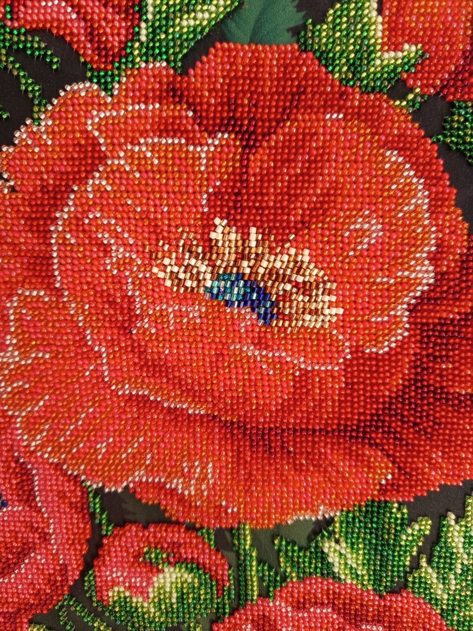 Macro detail of a large red poppy embroidered with coral, scarlet, gold and blue glass beads